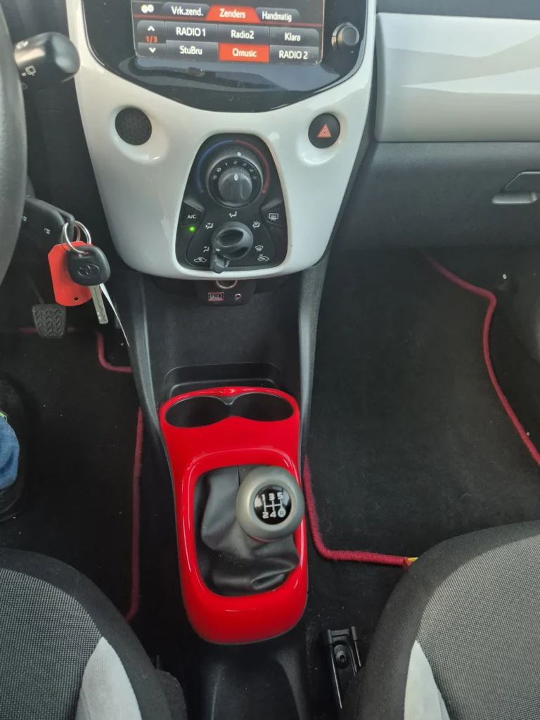 Dashboard en versnellingspook van een auto met rode accenten.