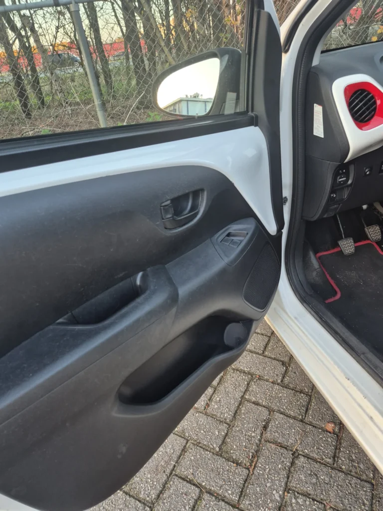 Interieur van een autodeur met zicht op het dashboard en pedalen.