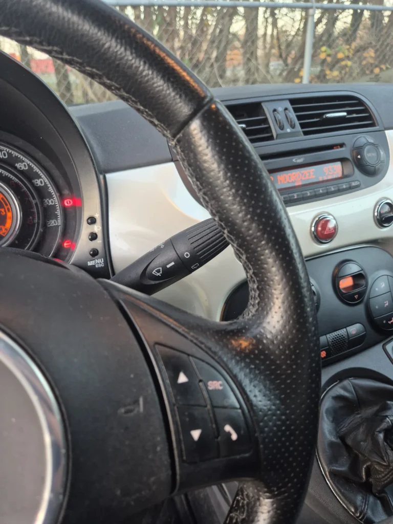 Stuurwiel en dashboard van een auto met knoppen en meters.