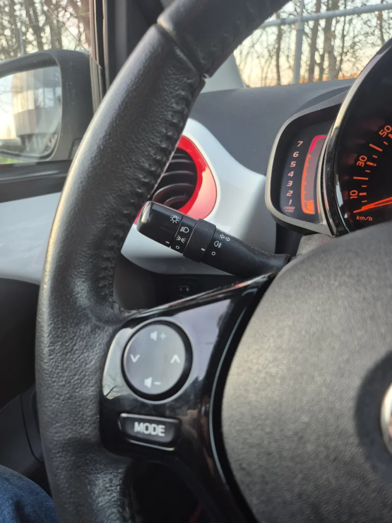 Stuurwiel en dashboard van een auto met zicht op snelheidsmeter en bedieningsknoppen.