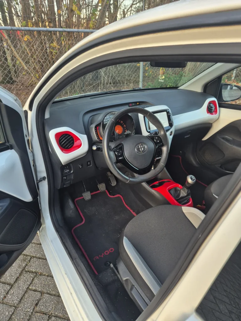 Stuur en dashboard van een compacte auto met rode accenten.
