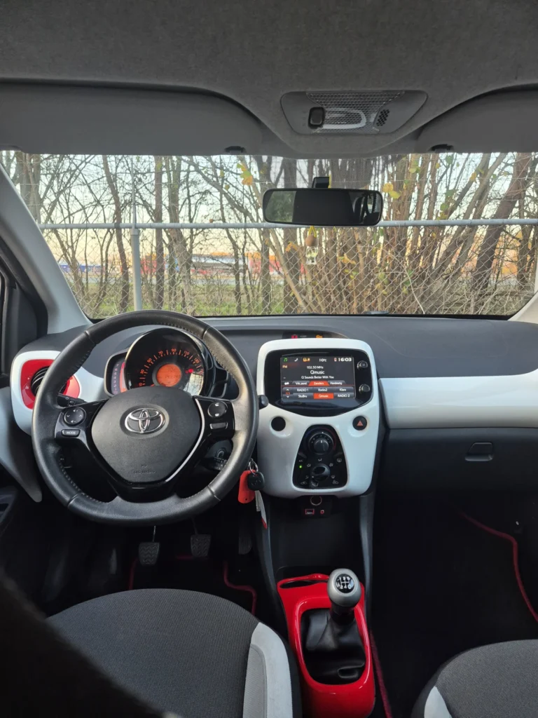 Stuurwiel en dashboard van een auto met een scherm en versnellingspook.