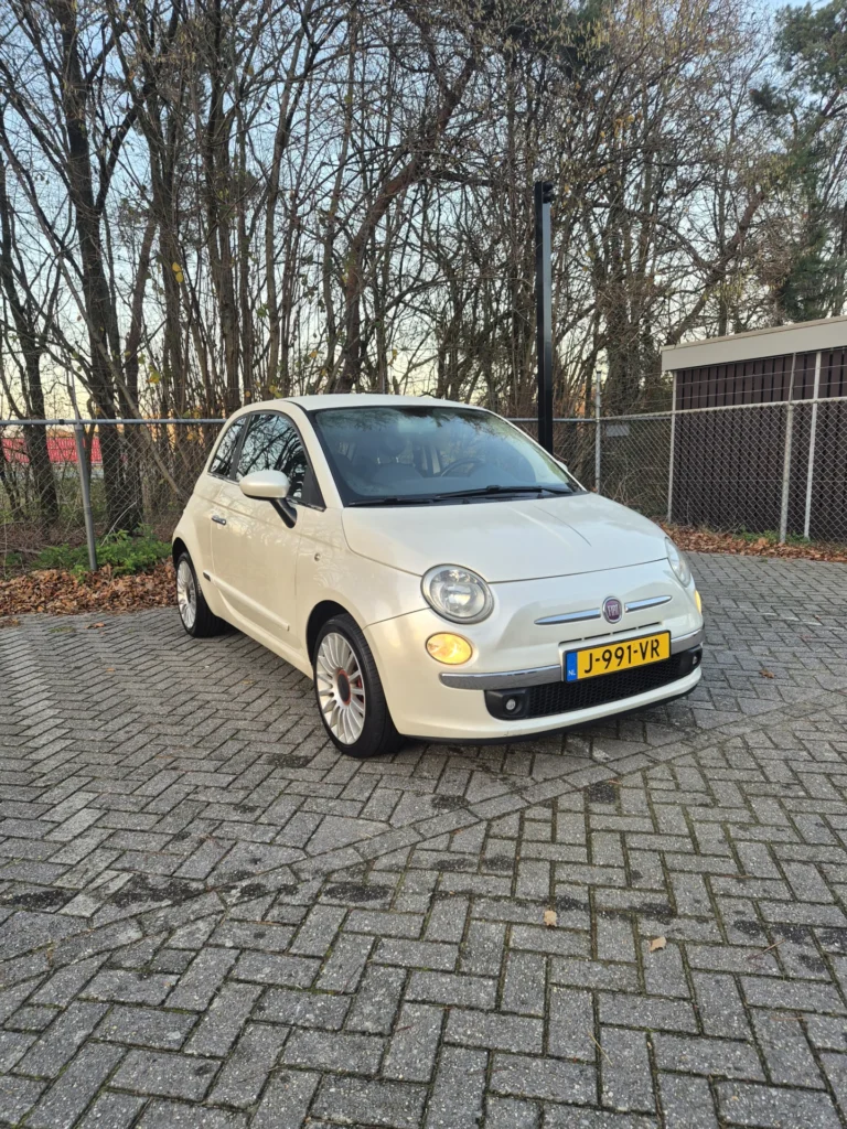 Witte auto geparkeerd op een stenen parkeerplaats naast een hek.