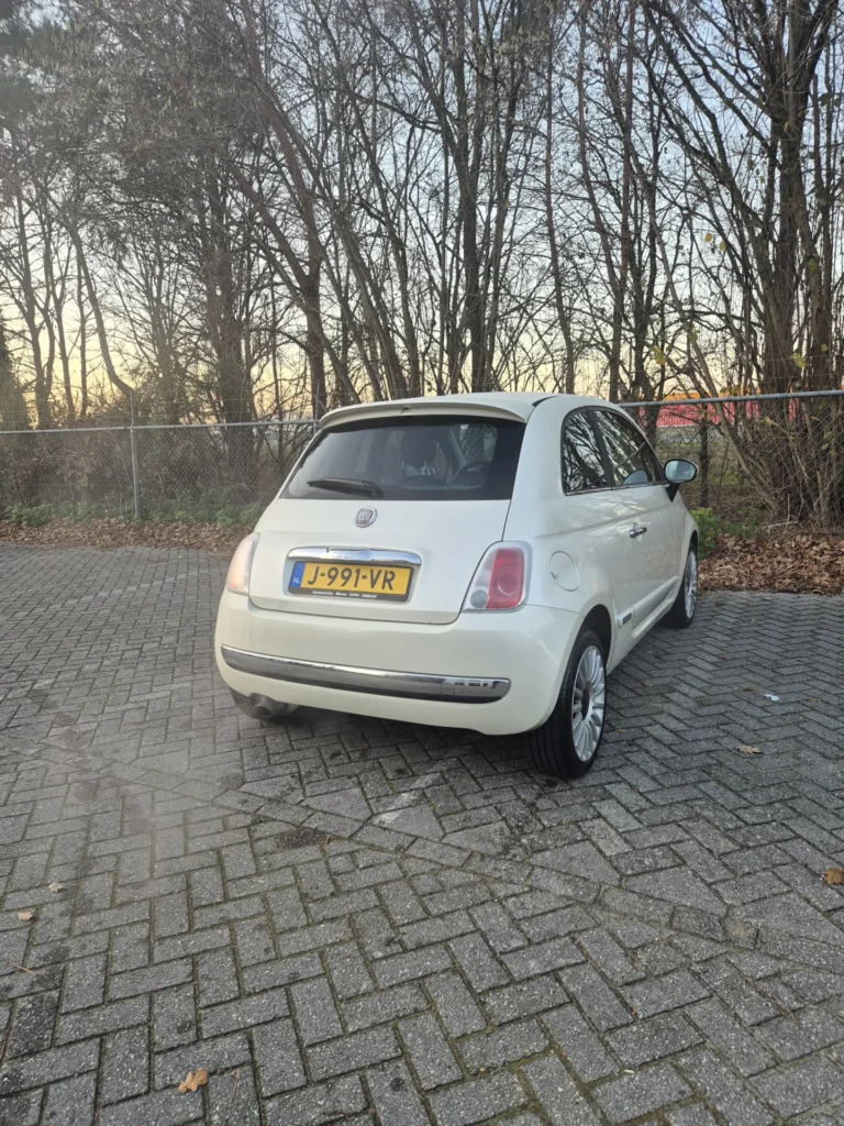 Witte auto geparkeerd op een stenen parkeerplaats naast bomen.
