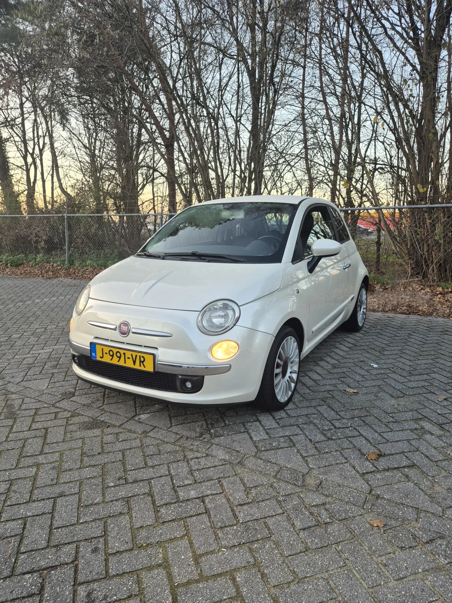 Witte auto geparkeerd op een stenen parkeerplaats bij bomen.