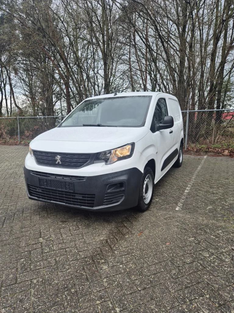 Witte bestelwagen geparkeerd op een stenen parkeerplaats met bomen op de achtergrond.