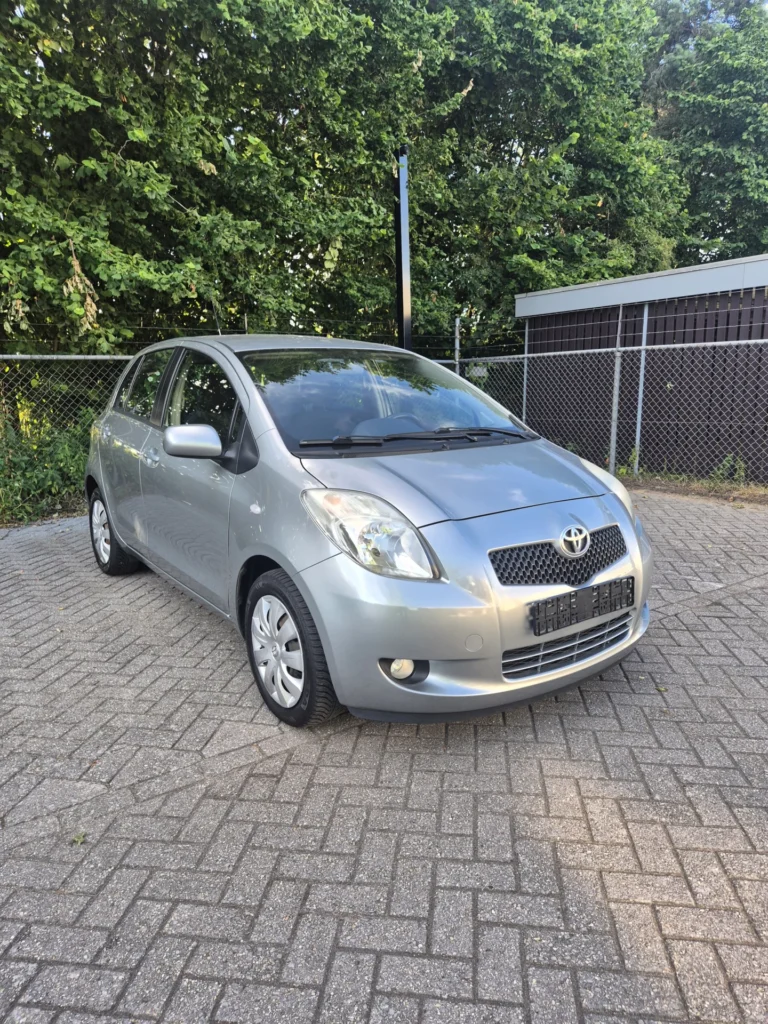 Zilveren Toyota auto geparkeerd op een betegelde parkeerplaats naast een hek.